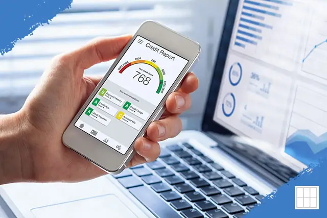 A hand holding a smartphone displaying a credit report with a 768 FICO score in the 'Good' range, with a laptop showing financial charts in the background.