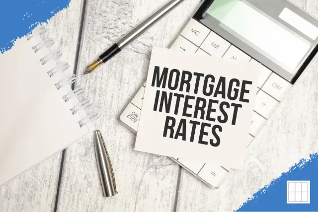 A wooden desk with a calculator, notebook, pen, and a card displaying the text 'MORTGAGE INTEREST RATES' for financial planning.