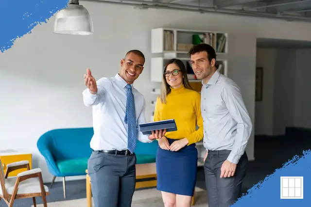 A real estate agent shows a modern living room to a smiling first-time home buyer couple during a property tour.