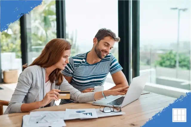 A smiling young couple sitting at their dining table, reviewing mortgage documents and using a laptop to research how to cancel PMI on their conventional loan in Overland Park, Kansas.