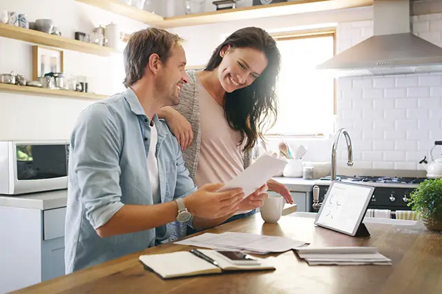 Happy couple sitting in a modern kitchen, reviewing financial documents and using a tablet computer to calculate their Kansas City home affordability budget.