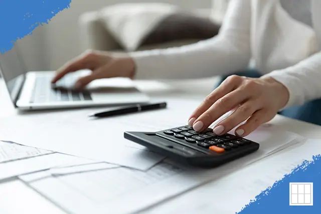 Close-up of a person using a calculator and laptop to review financial documents, illustrating the management of a mortgage impound account.